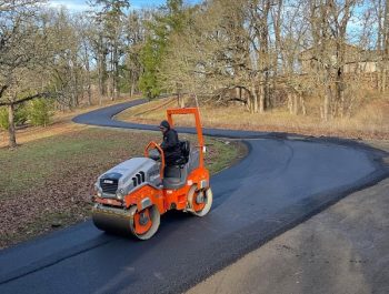 A Legacy Paving contractor smooths fresh road pavement in a quiet, tree-lined neighborhood. A Legacy Paving contractor smooths fresh road pavement in a quiet, tree-lined neighborhood.
